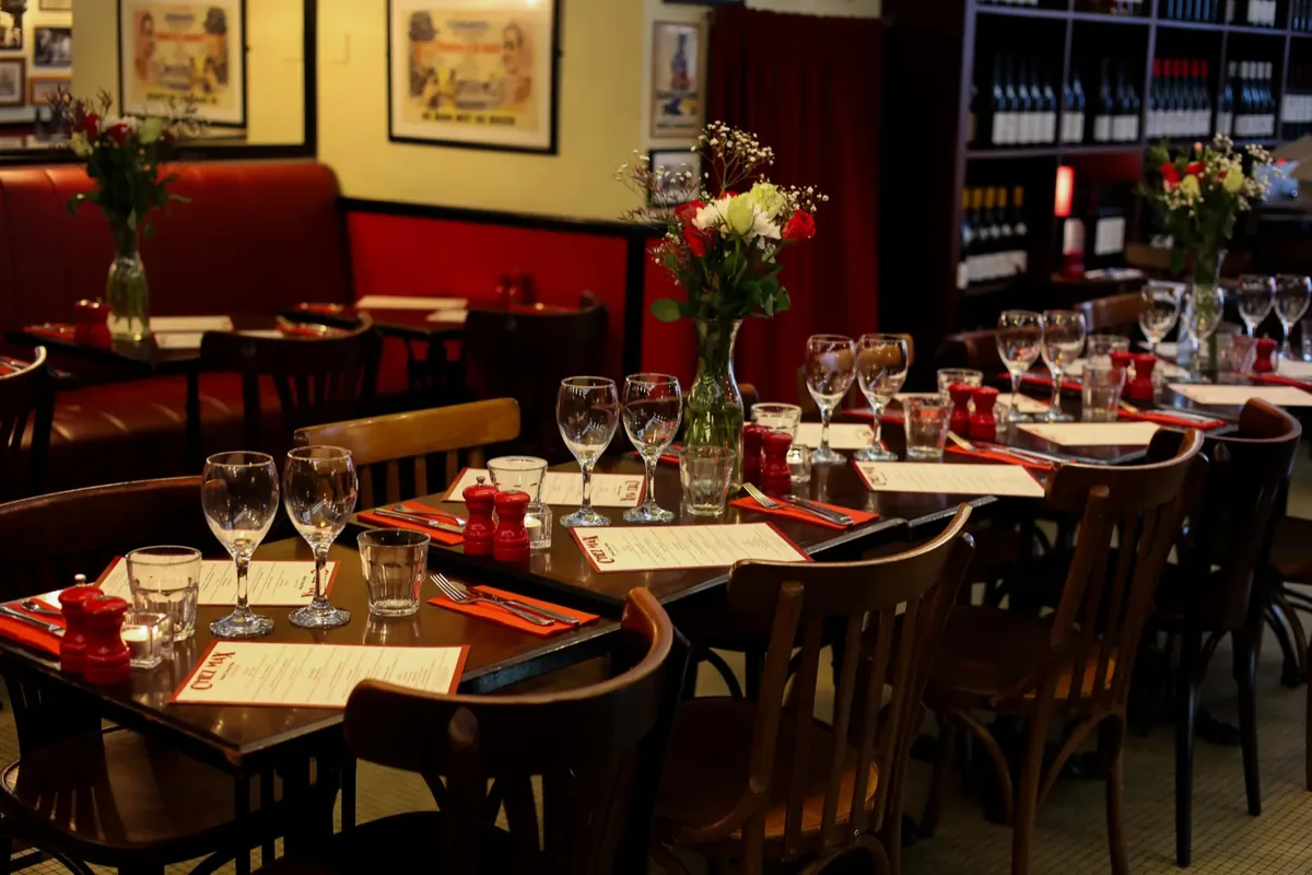 Tables set with menus and fresh flowers in the Chez Max dining room, French wine shelves behind