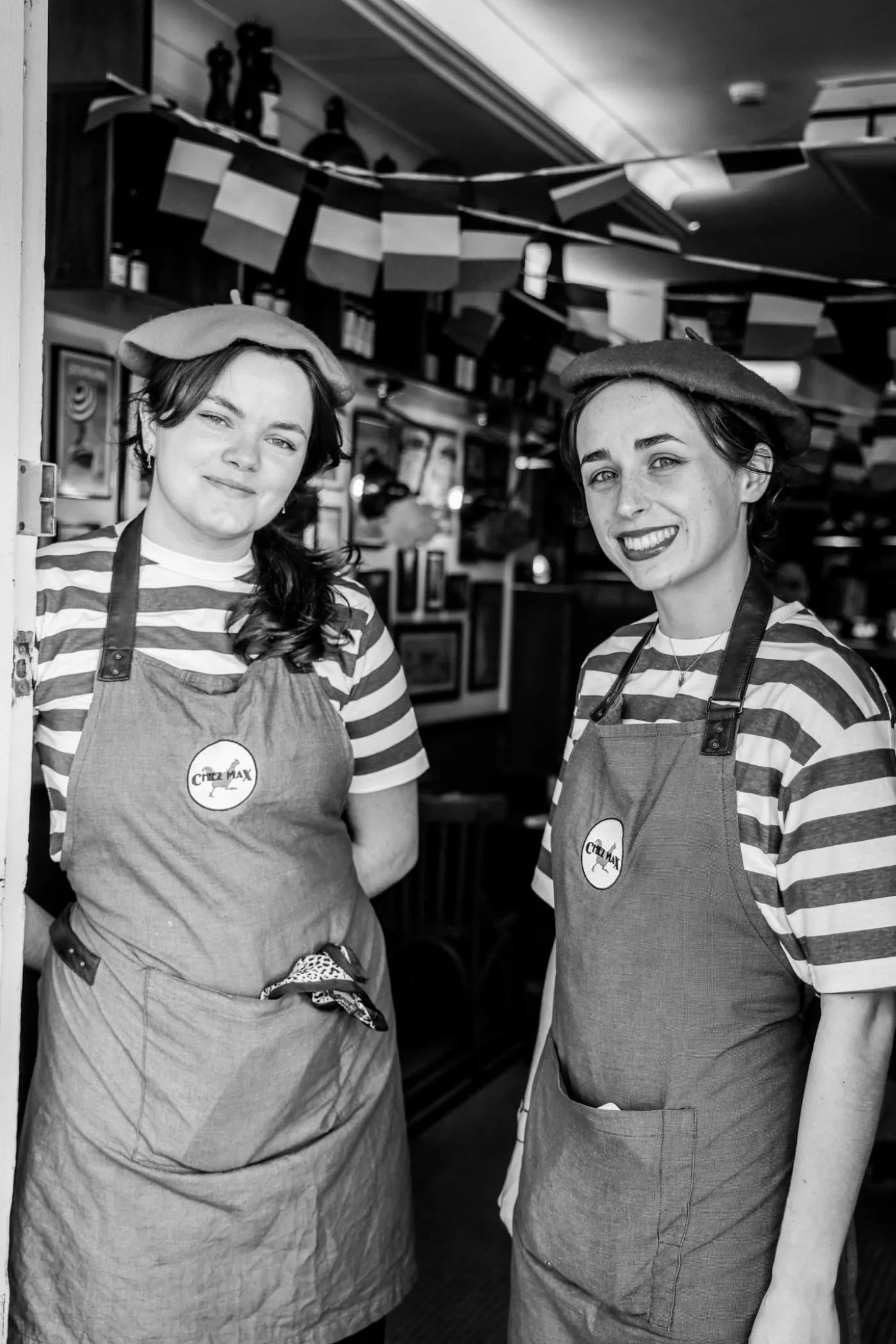 Two of the team in berets and striped tops, smiling in the doorway