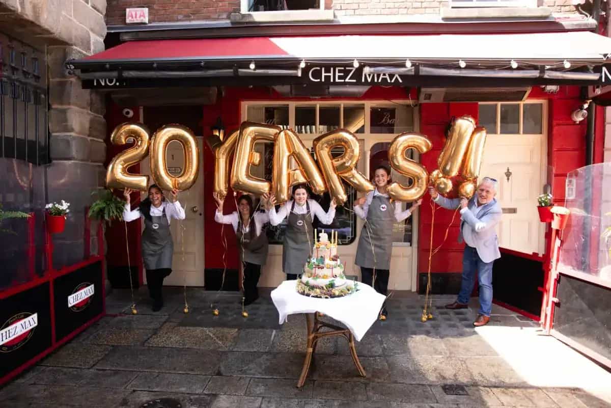 The Chez Max team holding golden “20 years” balloons in front of the restaurant on Palace Street