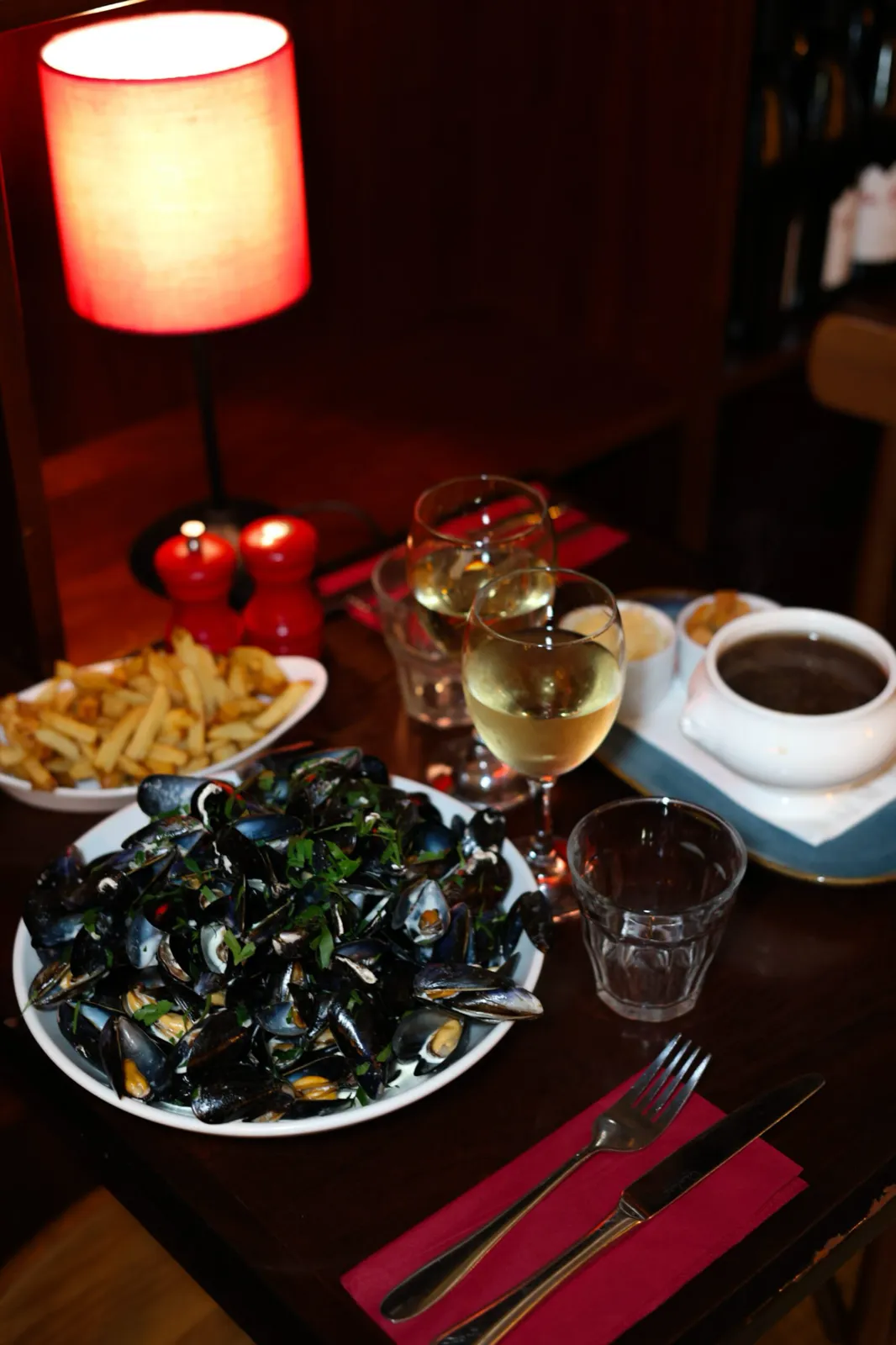 Moules marinières with parsley, frites maison and a glass of white wine under a red lamp